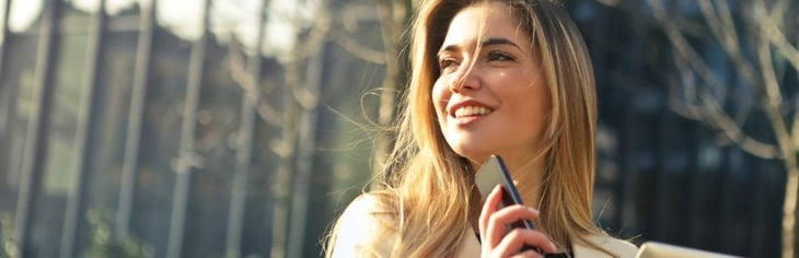 En leende kvinna som håller i en telefon och en padda, content marketing
